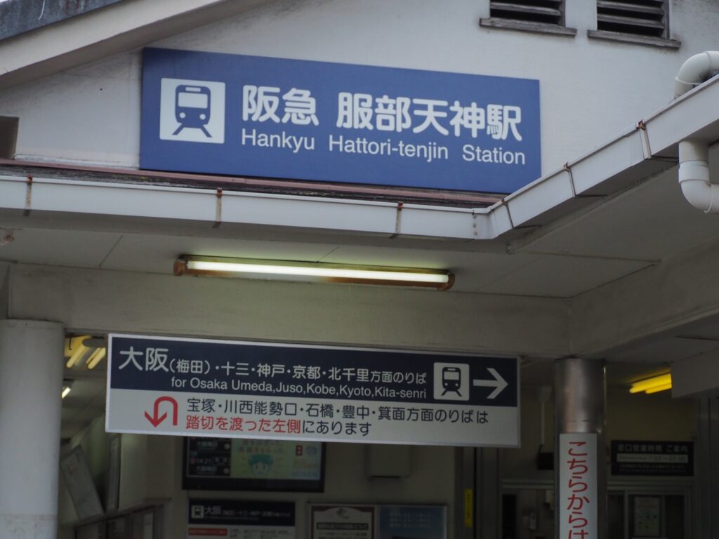 阪急服部天神駅の駅舎と、踏切を渡る乗り場案内