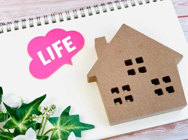 ノートの上に置かれた木の家のオブジェとピンク色の「LIFE」の付箋
