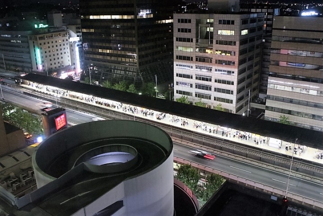 ビル群に囲まれた夜の御堂筋線・江坂駅と周辺の街並みを高所から見下ろした夜景
