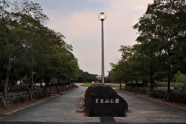 「紫金山公園」と彫られた大きな石の銘板と緑豊かなアプローチ