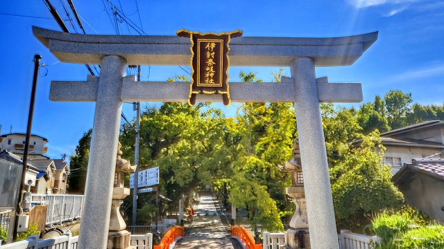 青空のもとに佇む石の鳥居と朱色の橋、緑豊かな境内の風景
