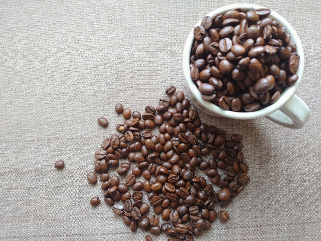 カップに入ったコーヒー豆とデスク上に広がる焙煎豆の風景
