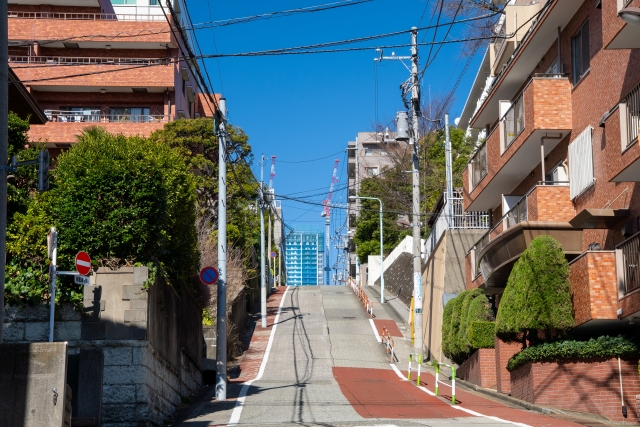 青空のもとに続く坂道とレンガ造りの建物が並ぶ住宅街の風景

