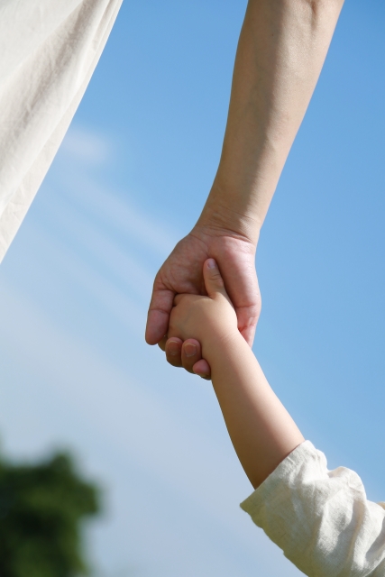 青空のもとでしっかりと手をつなぐ親と子の手元
